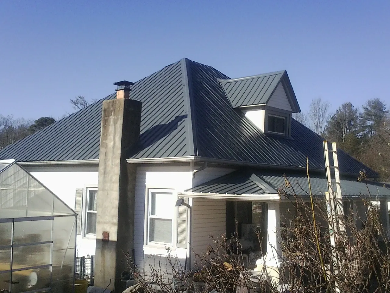 Dark blue standing seam metal roof on a white farmhouse with dormer — Slate & Tile Roof Repair by Roofing Brothers in Le Mars