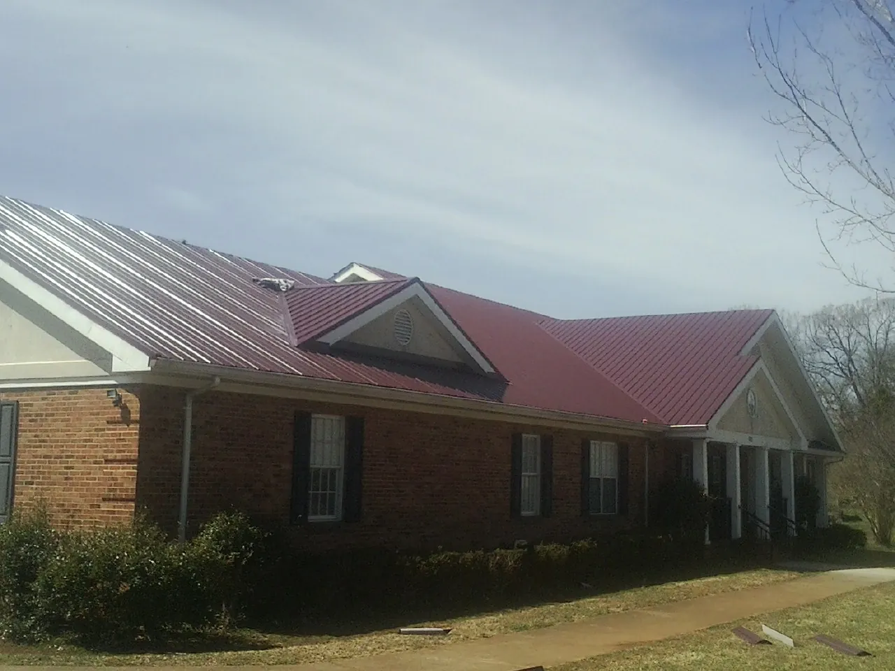 Red metal roof with gabled entries on a long brick building, from a Hail Damage Roof Repair job in Le Mars