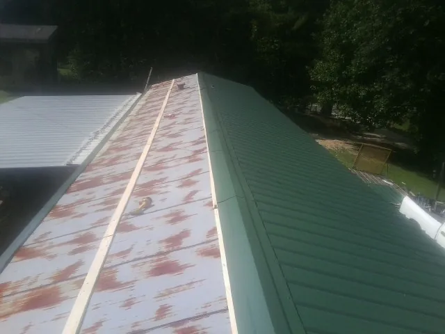 Old rusted panels beside newly installed green metal roofing — Wind Damage Roof Repair by Roofing Brothers in Le Mars