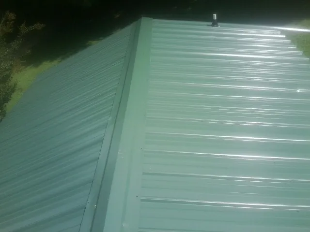 New green metal panels meeting at the ridge of a roof — Flat Roof Repair work by our crew in Le Mars