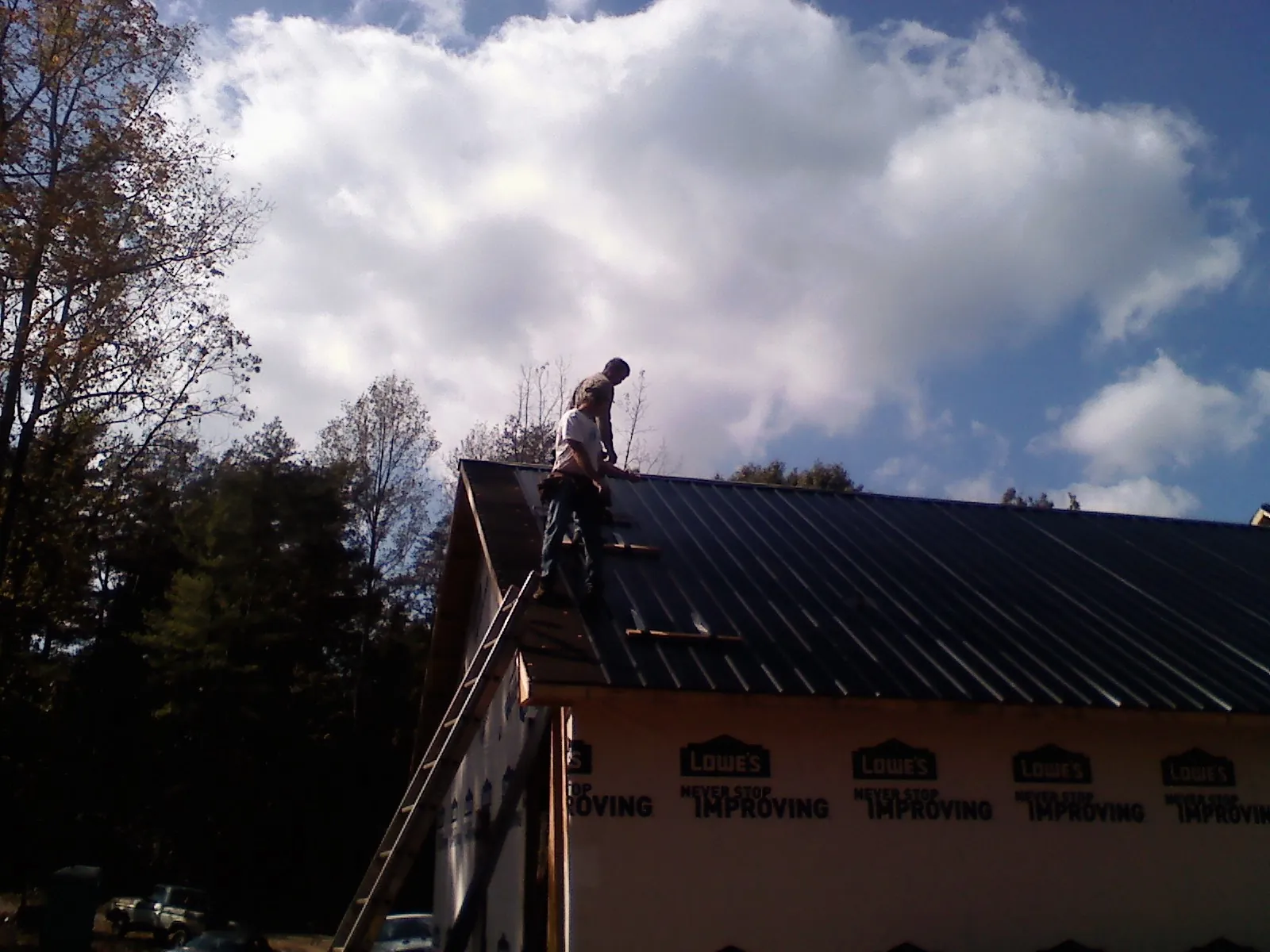 Roofer fastening dark metal panels high against a cloudy sky, from a Roof Inspection job in Le Mars