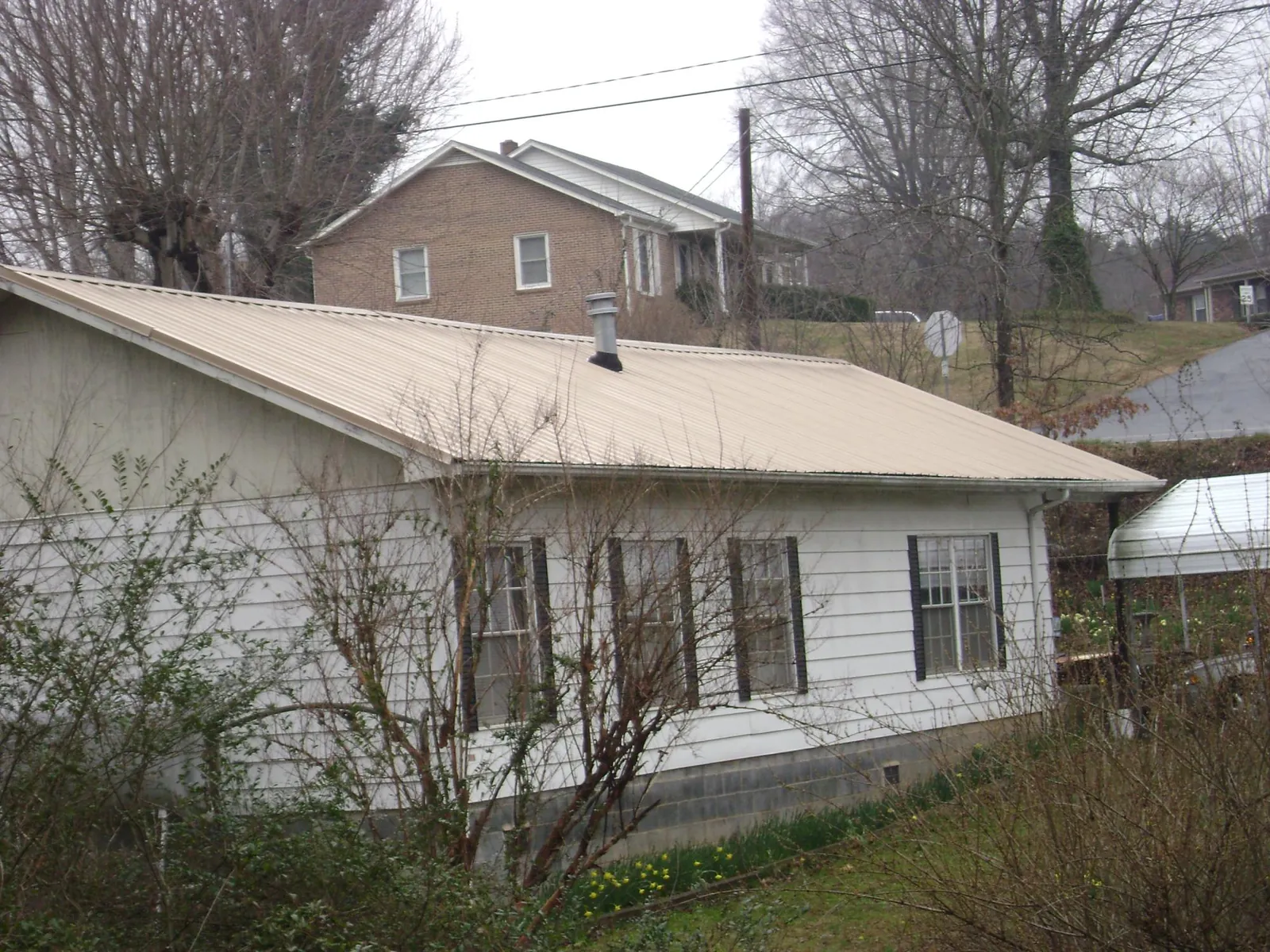 Tan metal roof on a white sided house set into a hillside in Le Mars